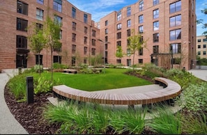 A multi-story building with a courtyard featuring a circular wooden bench, greenery, and a clear sky. - The Pullman Suite - near train station (York)