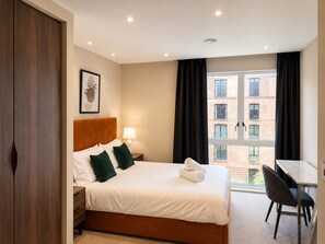 A hotel room with a bed, bedside table, lamp, and a view of the outside. - The Pullman Suite - near train station (York)