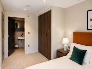 A hotel room with a bed, a nightstand, a bedside lamp, a wardrobe, and a bathroom visible through an open door. - The Pullman Suite - near train station (York)