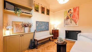 A room with a wooden herringbone floor, a bench, a guitar, a radiator, and a painting on the wall.