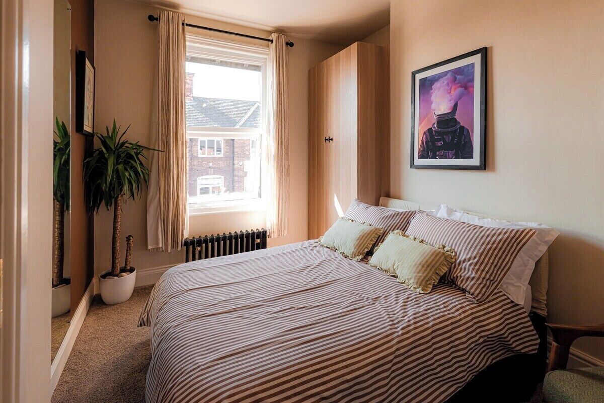 Une chambre à coucher avec un lit, une fenêtre, un radiateur, une plante en pot et un tableau encadré au mur.