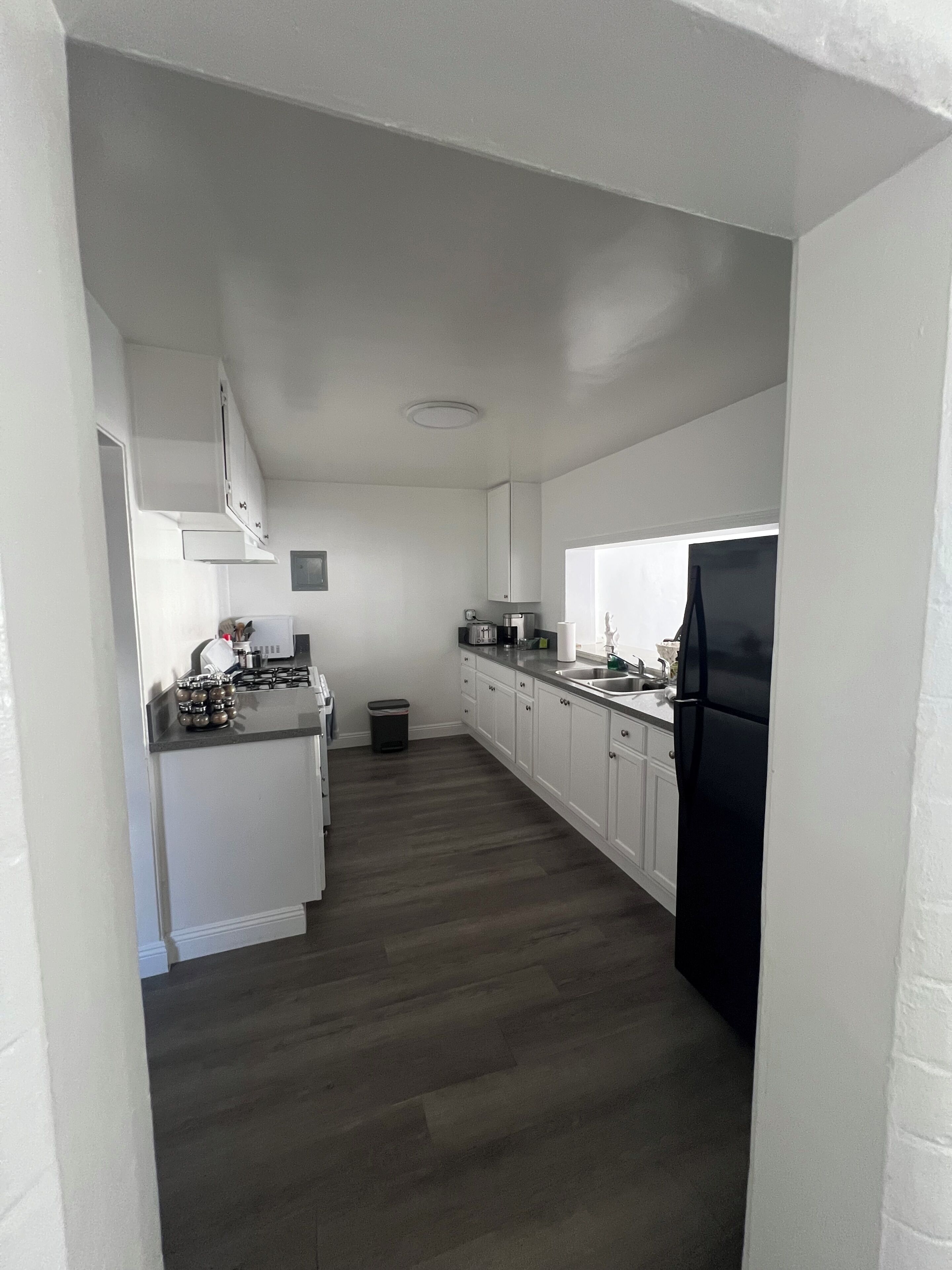 Una cocina con armarios blancos, un refrigerador negro y una encimera gris.