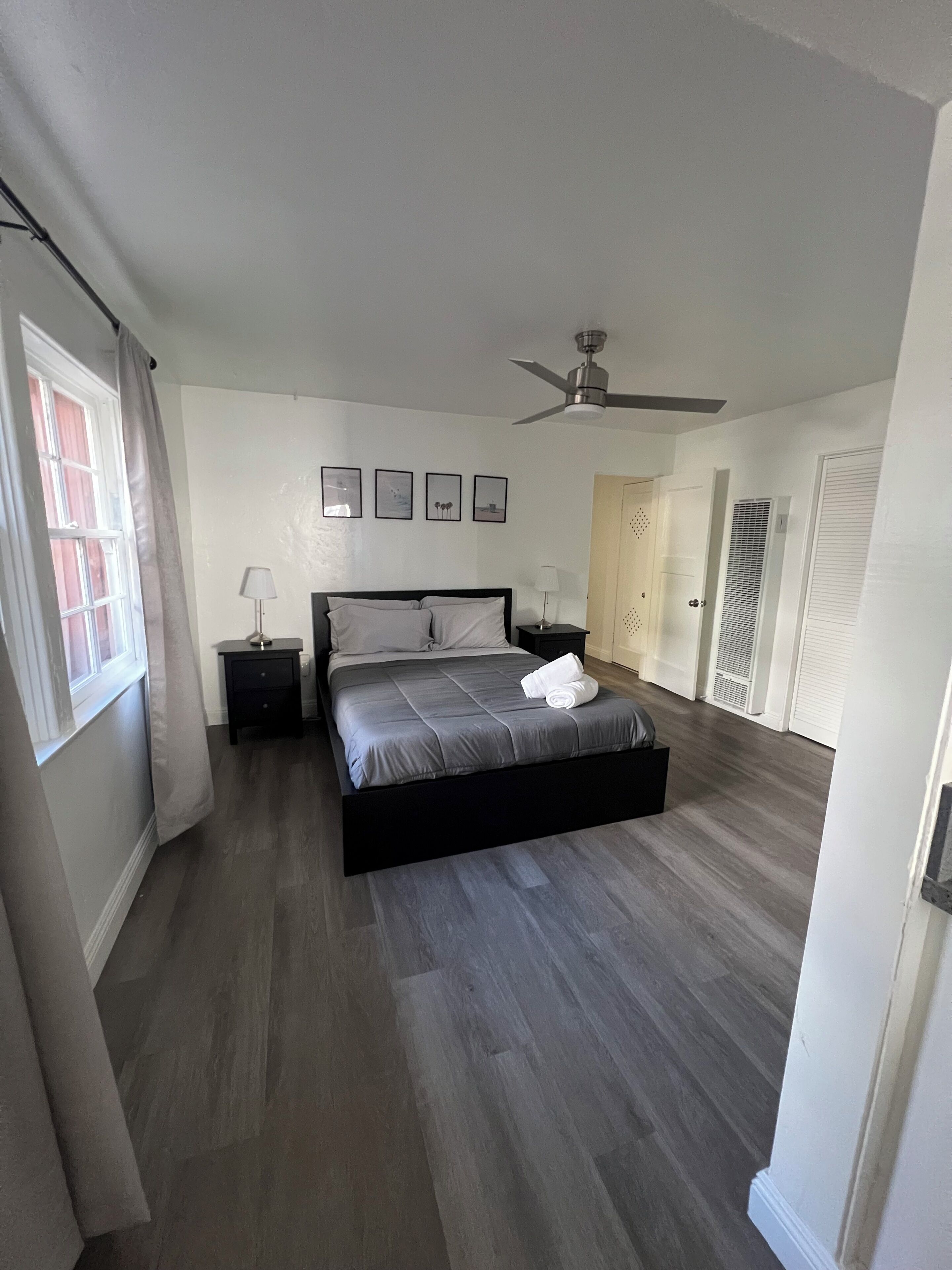 Une chambre à coucher avec un lit, une table de chevet, un ventilateur de plafond et une fenêtre avec des rideaux.