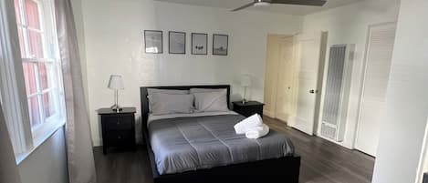 Une chambre à coucher avec un lit, une table de chevet, un ventilateur de plafond et une fenêtre avec des rideaux.