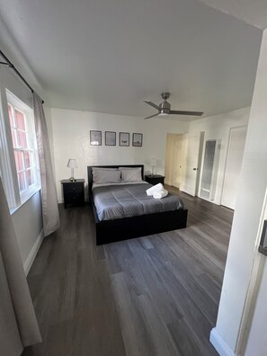 A bedroom with a bed, a nightstand, a ceiling fan, and a window with curtains. - Peaceful 2BR Carlsbad condo just 1½ blocks from the beach (Carlsbad)