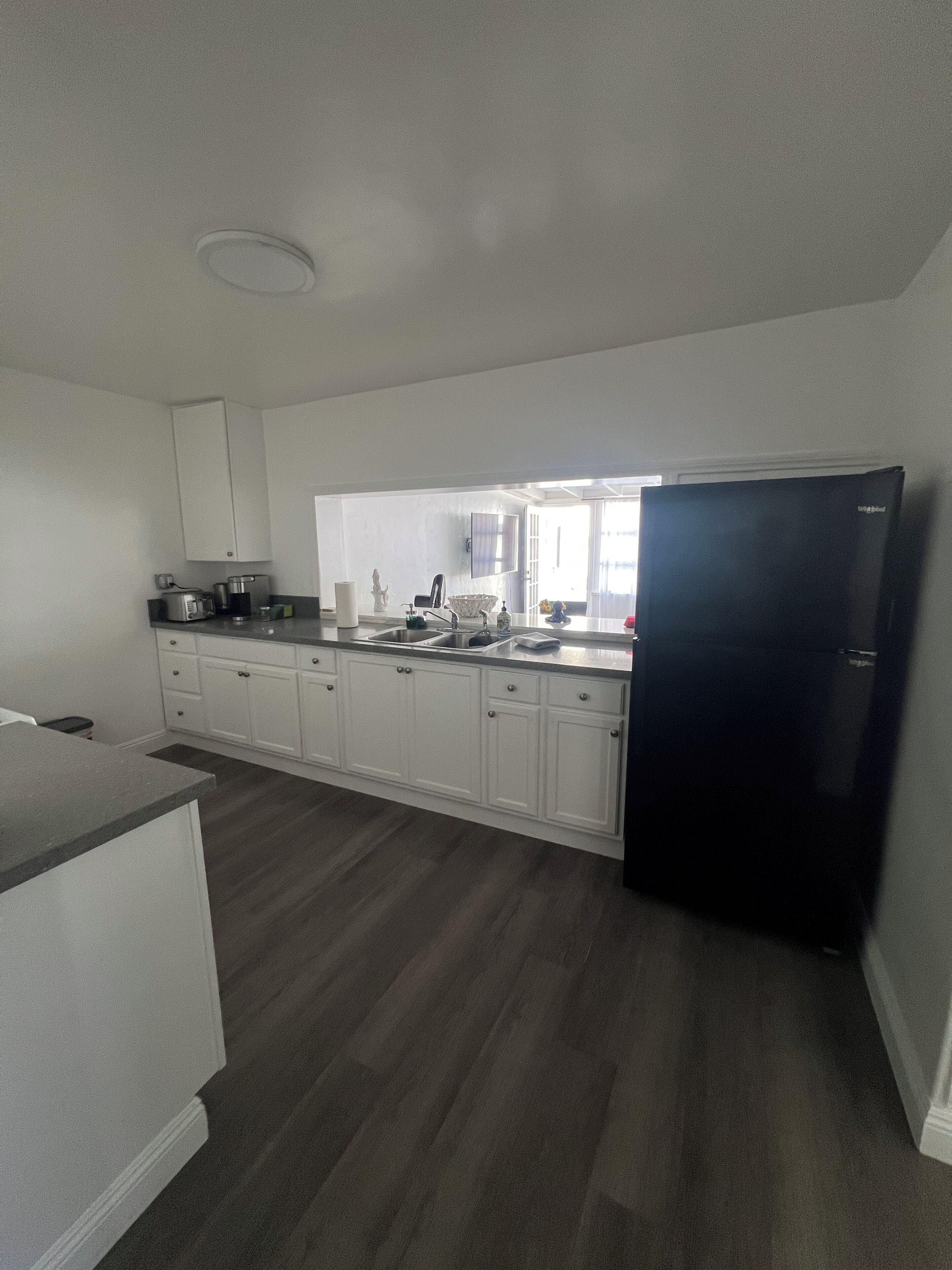 A kitchen with white cabinets, a black refrigerator, and a wooden floor.