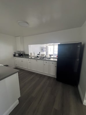 A kitchen with white cabinets, a black refrigerator, and a wooden floor.