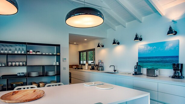 A modern kitchen with a dining area, featuring a white table, blue cabinets, and a large window with a view of the ocean. - Villa Summertime (2 bedrooms) (Saint Barthélemy)