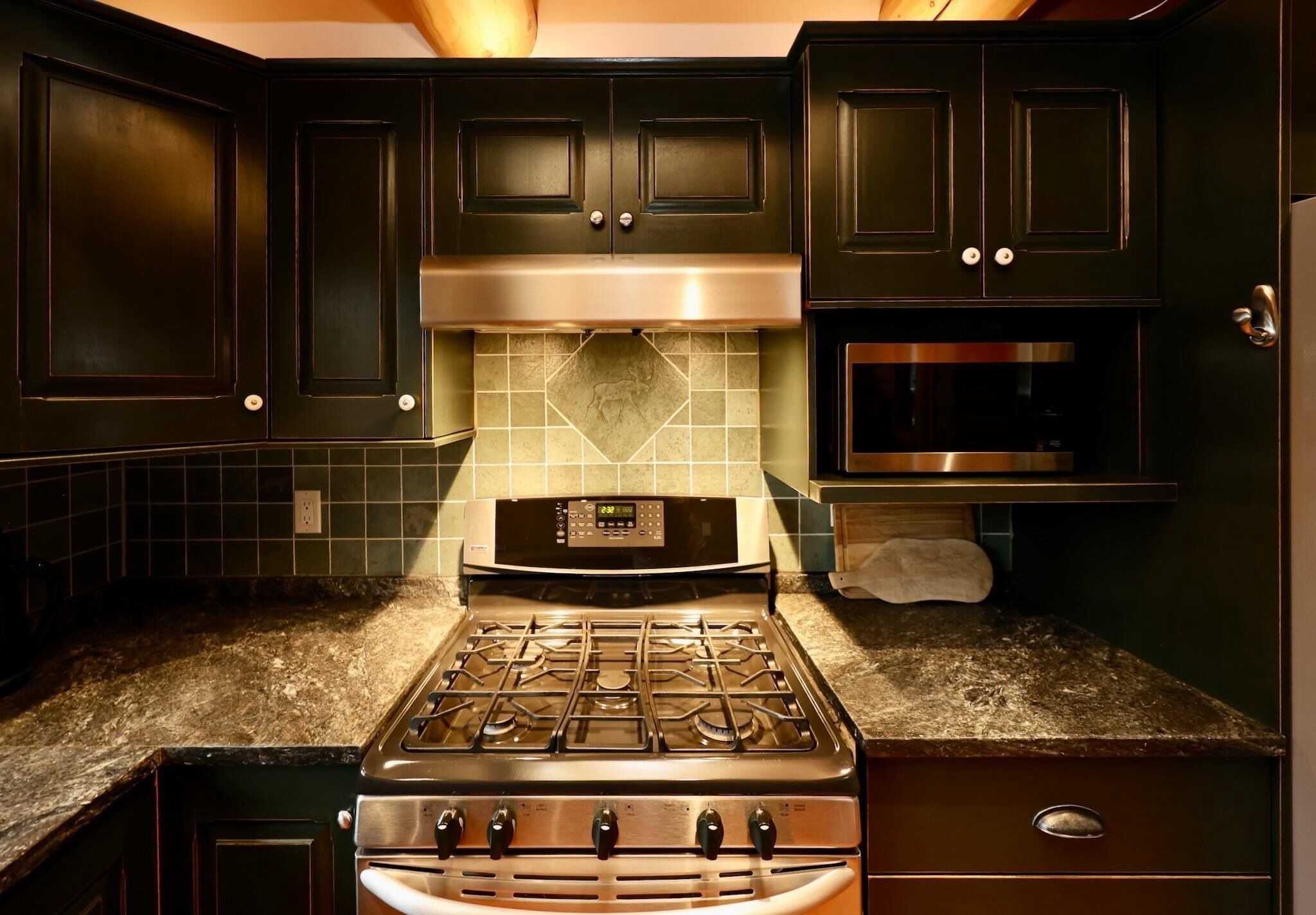 A kitchen with dark cabinets, a stainless steel stove, and a microwave.
