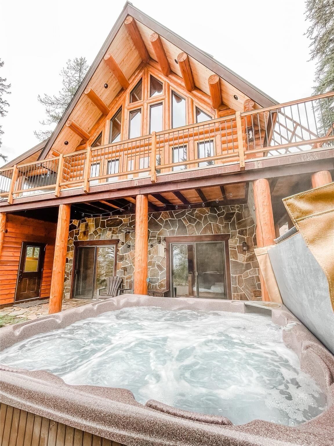 A log cabin with a hot tub, stone walls, and a balcony.