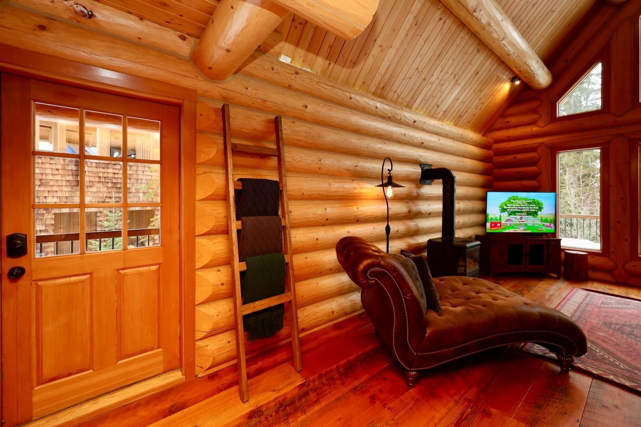 A log cabin interior with a wooden door, a fireplace, a leather sofa, and a television.
