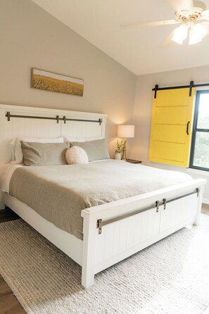 A bedroom with a bed, a nightstand, a lamp, a ceiling fan, and a window with a yellow door. - Cozy 3-Level Chattanooga Retreat with Relaxing Outdoor Spaces (Chattanooga)
