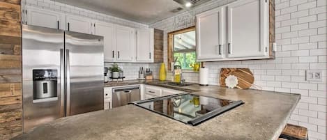 A kitchen with white cabinets, a stainless steel refrigerator, a built-in oven, and a wooden accent wall.