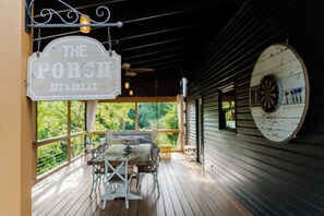 A porch area with a sign reading 'The Porch Sit & Relax,' a dartboard, and a table with chairs. - Cozy 3-Level Chattanooga Retreat with Relaxing Outdoor Spaces (Chattanooga)