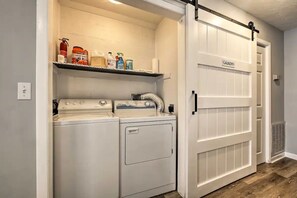 A laundry area with a white door labeled 'LAUNDRY,' a shelf with cleaning supplies, and a dryer. - Cozy 3-Level Chattanooga Retreat with Relaxing Outdoor Spaces (Chattanooga)