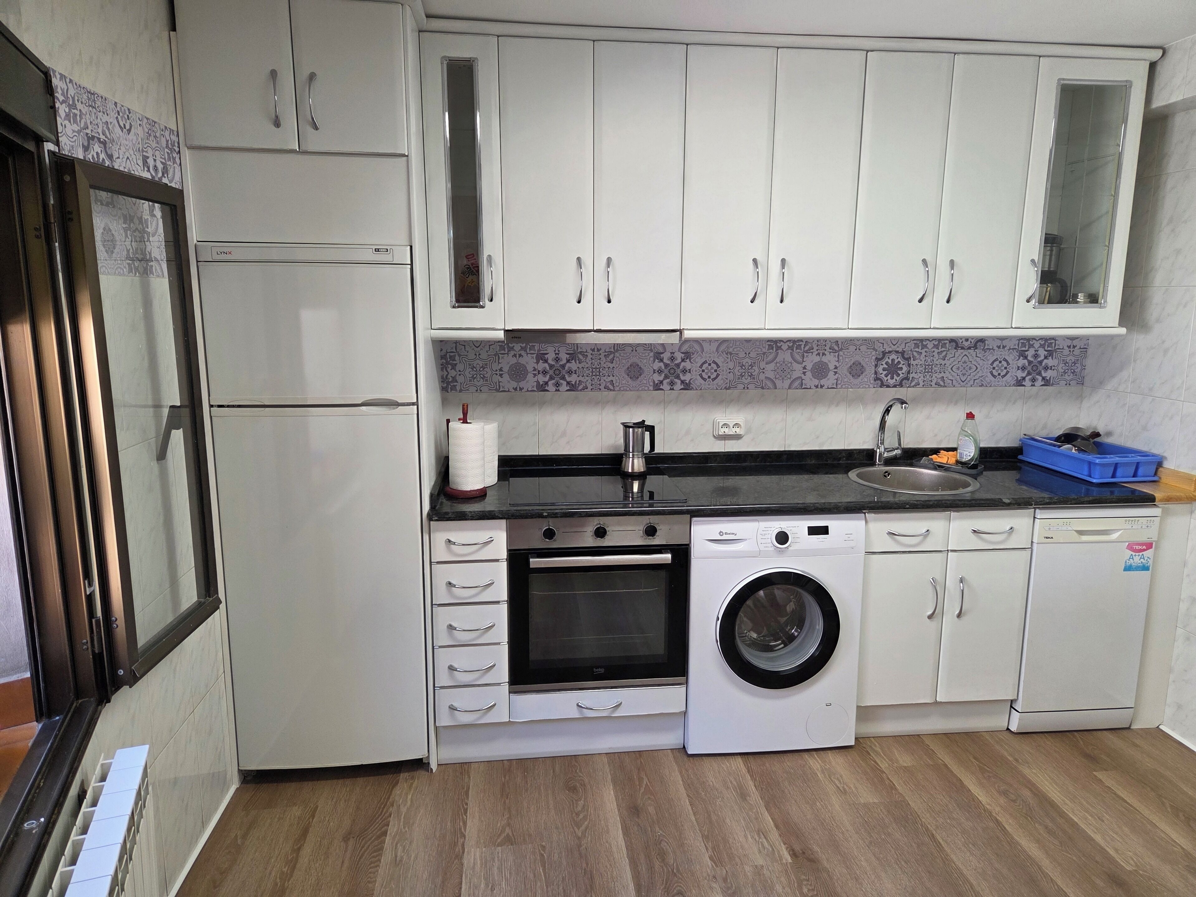 A compact kitchen with white cabinets, a built-in oven, a washing machine, and a sink.