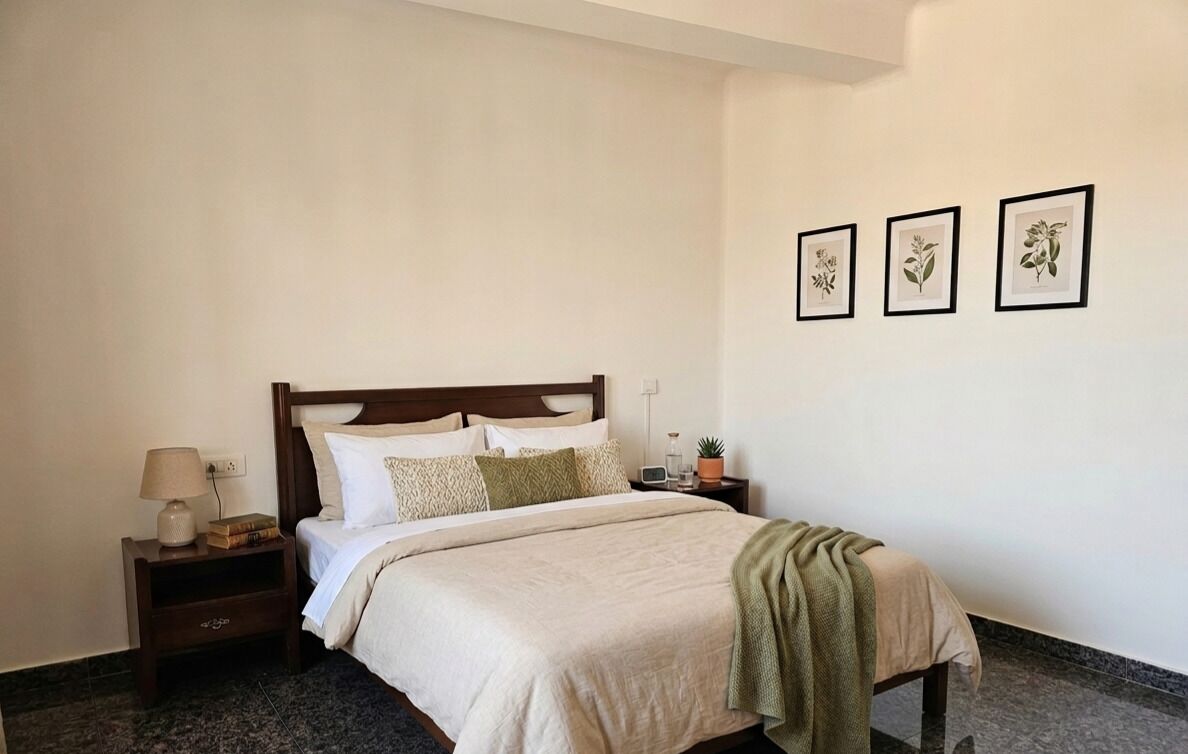 Una camera da letto con un letto, un comodino, una lampada e tre stampe botaniche incorniciate alle pareti.