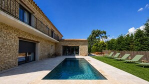 Une maison moderne dotée d’une piscine, d’une façade en pierre et d’une pelouse bien entretenue.