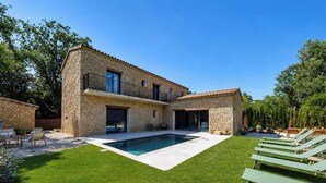 Une maison en pierre à deux étages, dotée d’une piscine, d’un espace salon extérieur et d’une pelouse bien entretenue.