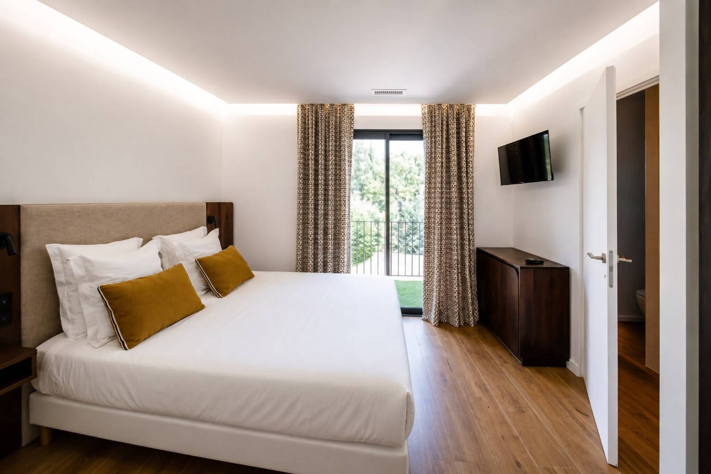 Ein Hotelzimmer mit einem großen Bett, einem flachbildfernseher an der Wand und Blick ins Freie durch das Fenster.