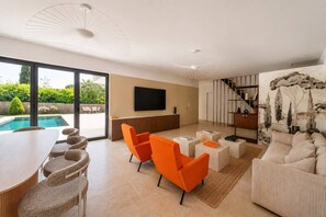 A modern living room with a pool view, a flat-screen TV, and a staircase leading to an upper level. - La Bâtisse - Piscine & Jardin - Luberon (Gordes)