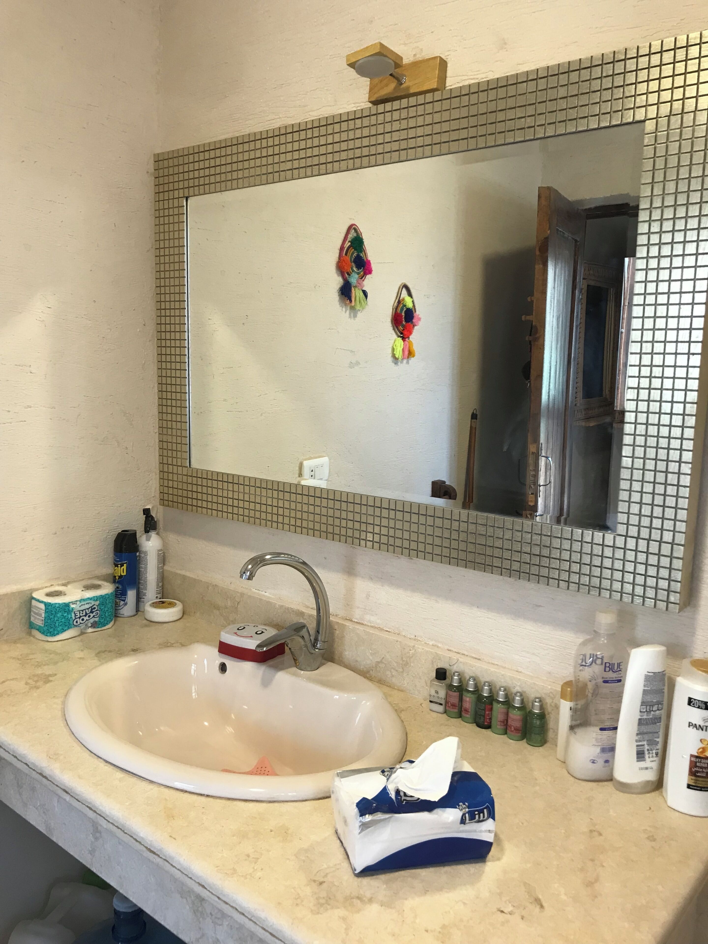 A bathroom with a white sink, a mirror with a grid pattern, and various toiletries on the counter.