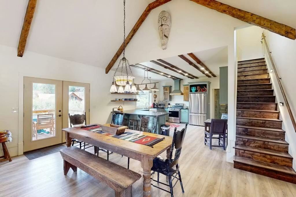 A spacious kitchen with modern appliances, a dining area with a wooden table, and a staircase with exposed wooden beams.