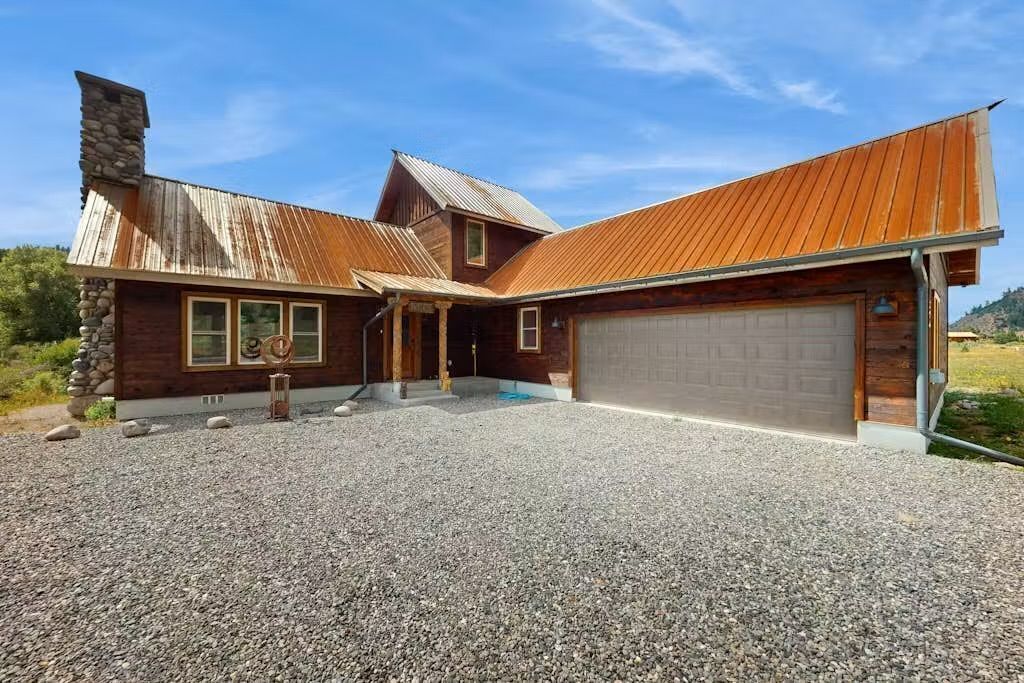 Une maison à deux étages avec un garage, une cheminée en pierre et une allée gravillonnée.