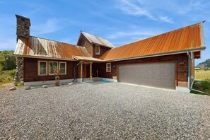 Ein zweistöckiges Haus mit Garage, einem Steinsschornstein und einem Schotterweg.