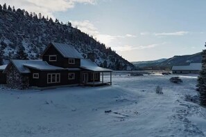 A cabin with a metal roof, surrounded by snow-covered ground and a forested hillside. - Pine Croft on Rio Grande  | 27 Mi to Wolf Creek (South Fork)