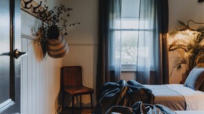 Een slaapkamer met een bed, een stoel, een hangplant en een raam met gordijnen.