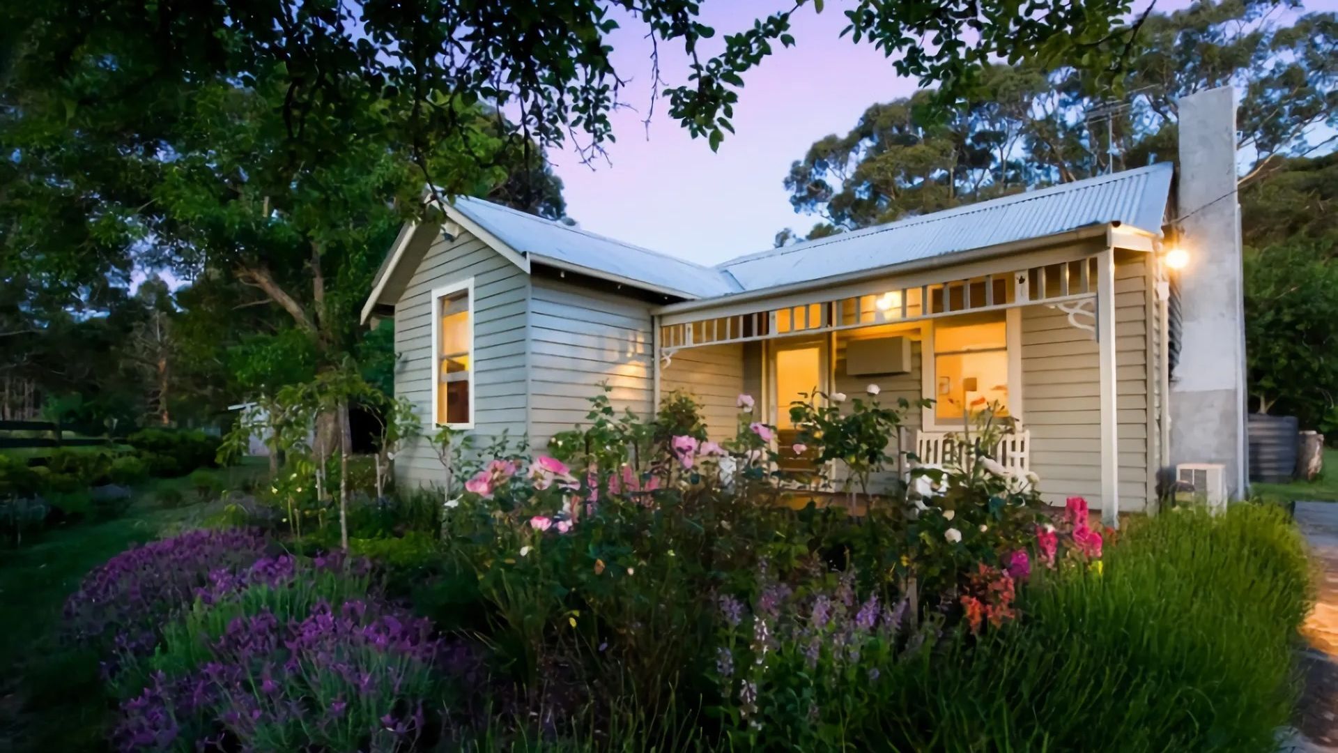 A single-story house with a porch, surrounded by lush vegetation and flowering plants.