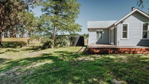 Ein eingeschossiges Haus mit Veranda, einer kleinen Gartenhütte und einem eingezäunten Garten.