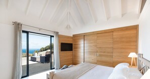 Ein Schlafzimmer mit einer großen Schiebeglasdoor zum Balkon, einem Holzschrank und einem Bett mit weißen Bettwäsche.