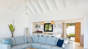 En moderne stue med en modulsofa, et køkken med hvide skabe og et stort vindue, samt et loft med et unikt geometrisk design.