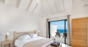 Ein Schlafzimmer mit einem Bett, Nachttischen und Meerblick durch eine Glastür.