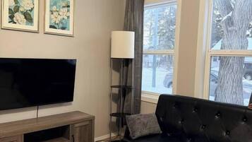 A living room with a flat-screen TV, a black sofa, a coffee table with a vase of flowers, and two framed floral paintings on the wall.