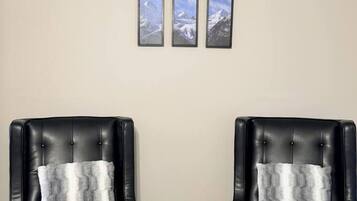 Deux fauteuils en cuir noir, dotés de coussins blancs, sont placés face à face, avec un mur beige en arrière-plan.