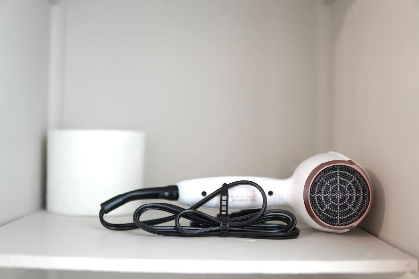 A hair dryer with a cord on a white shelf.