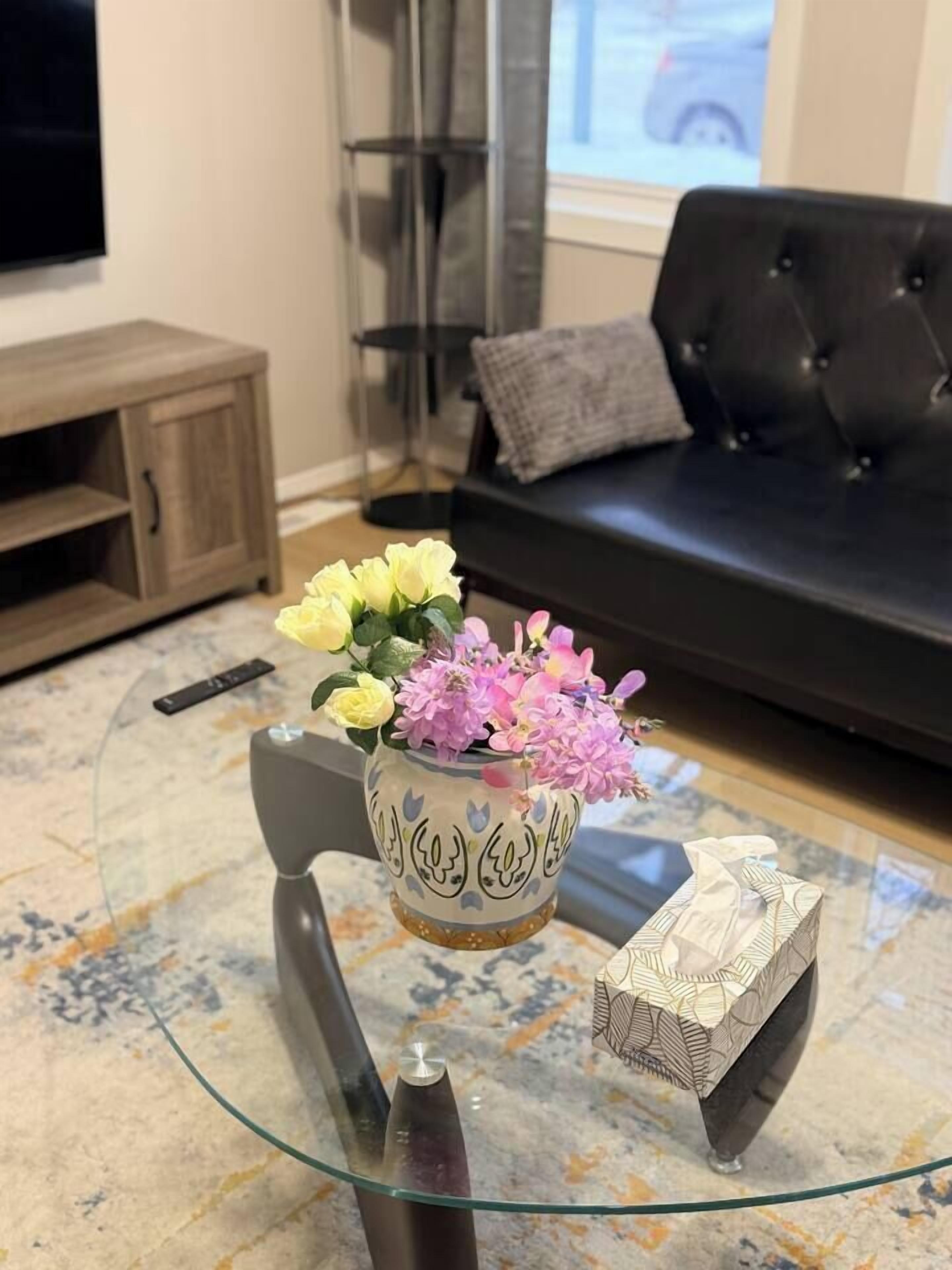 A glass coffee table with a vase of flowers, a remote control, and a decorative box.