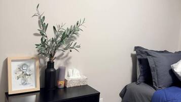 Une chambre à coucher avec un lit, une commode à tiroirs, un vase avec une plante, un tableau encadré et une peinture accrochée au mur.