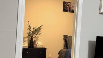 A room with a bed, a dresser, a wall-mounted TV, and a door leading to another room.