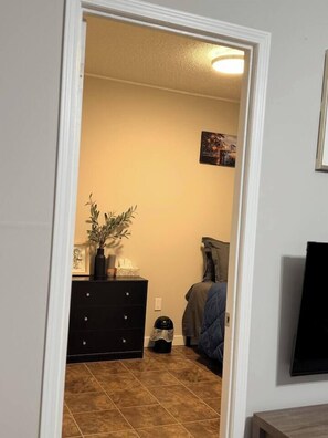 A room with a bed, a dresser, a wall-mounted TV, and a door leading to another room.