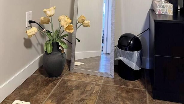 Un miroir avec un cadre argenté, un vase avec des fleurs jaunes et un objet noir sur une surface noire.