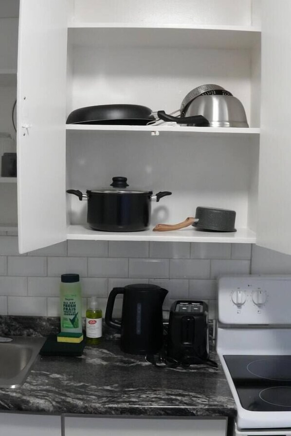 A kitchen with white cabinets, a stove, a coffee maker, and a bottle of dish soap.