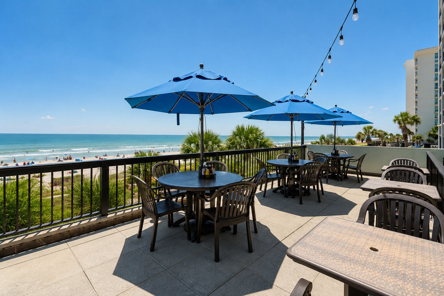 A terrace with tables and chairs, overlooking a beach.