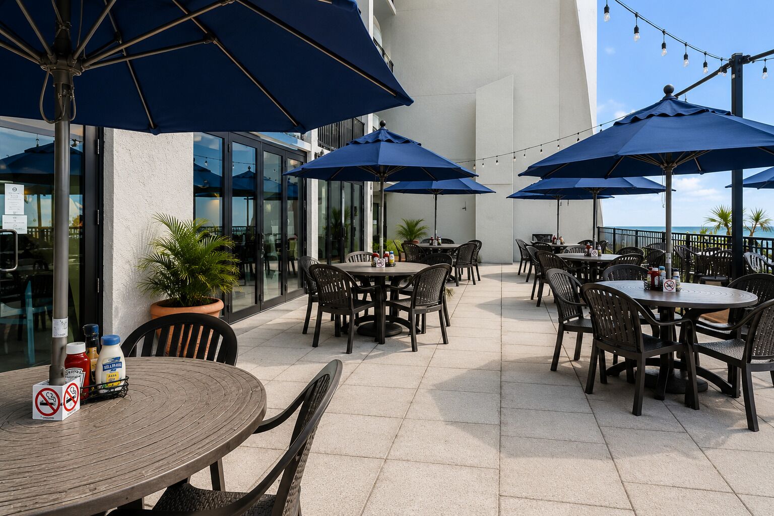 An outdoor patio area with round tables and chairs, covered by blue umbrellas, and a potted plant.