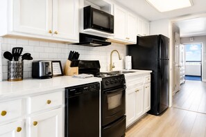 A modern kitchen with white cabinetry, a black refrigerator, a stainless steel stove, and a microwave. - The Peachy Palm Oceanfront at Compass Cove (Myrtle Beach)