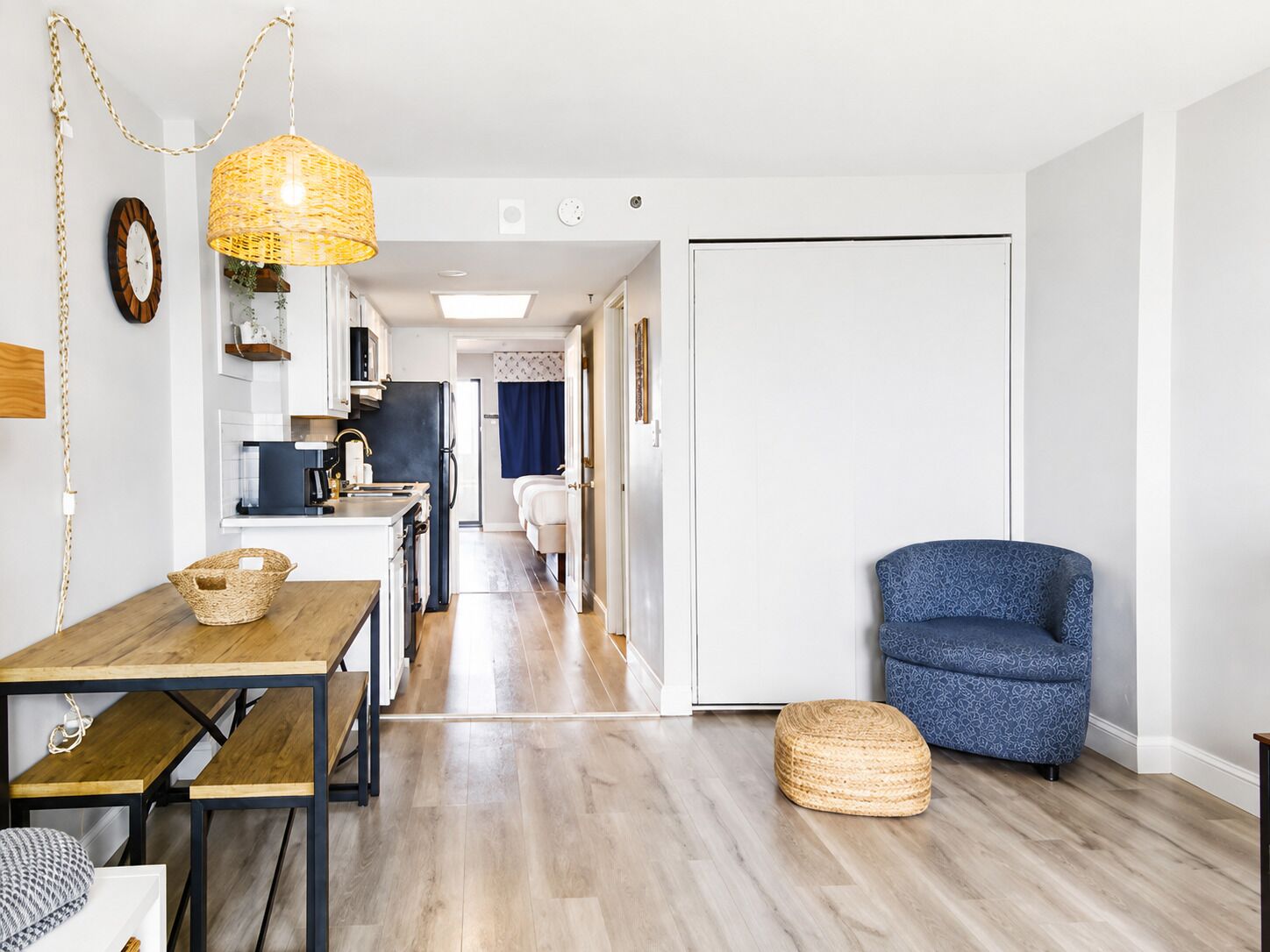 A modern kitchen with a dining area, a blue patterned chair, and a wicker basket on the floor.