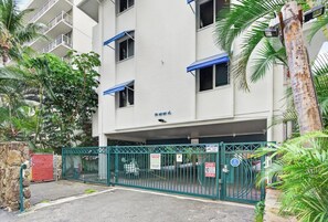 A multi-story building with a gated parking area, surrounded by greenery. - Cabana Waikiki Walk to Waikiki Beach With Free Parking Sleep for 4! (Honolulu)
